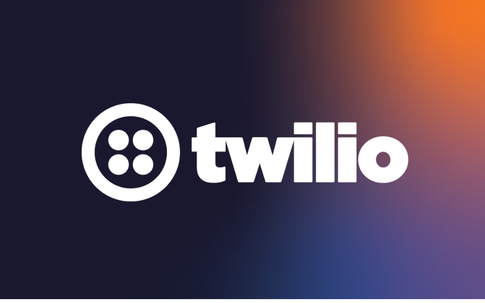 Logo of Twilio on a gradient background transitioning from dark blue on the left to orange on the right. The design includes a circular symbol with four dots next to the brand name in bold white letters.